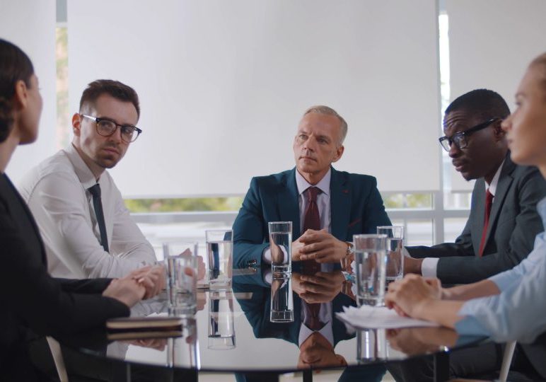 Business leader holding corporate meeting with team in boardroom. Multiracial business partners at meeting in conference room sitting at desk and discussing contract